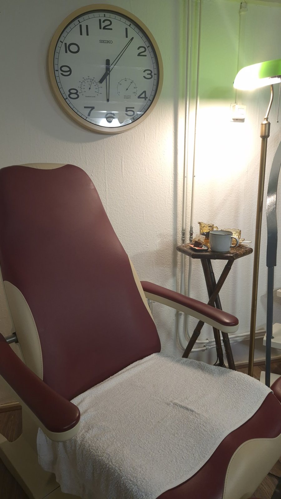 Behandelstoel met handdoek, een wandklok en een leeslamp in de salon